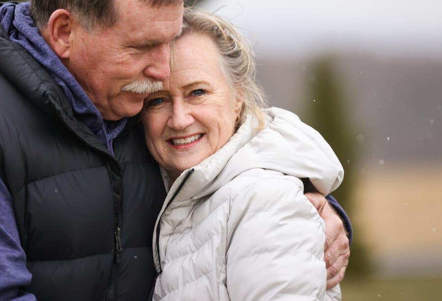 Tim McGinley (left) hugs his wife, Priscilla (right), outside of their home while snow falls