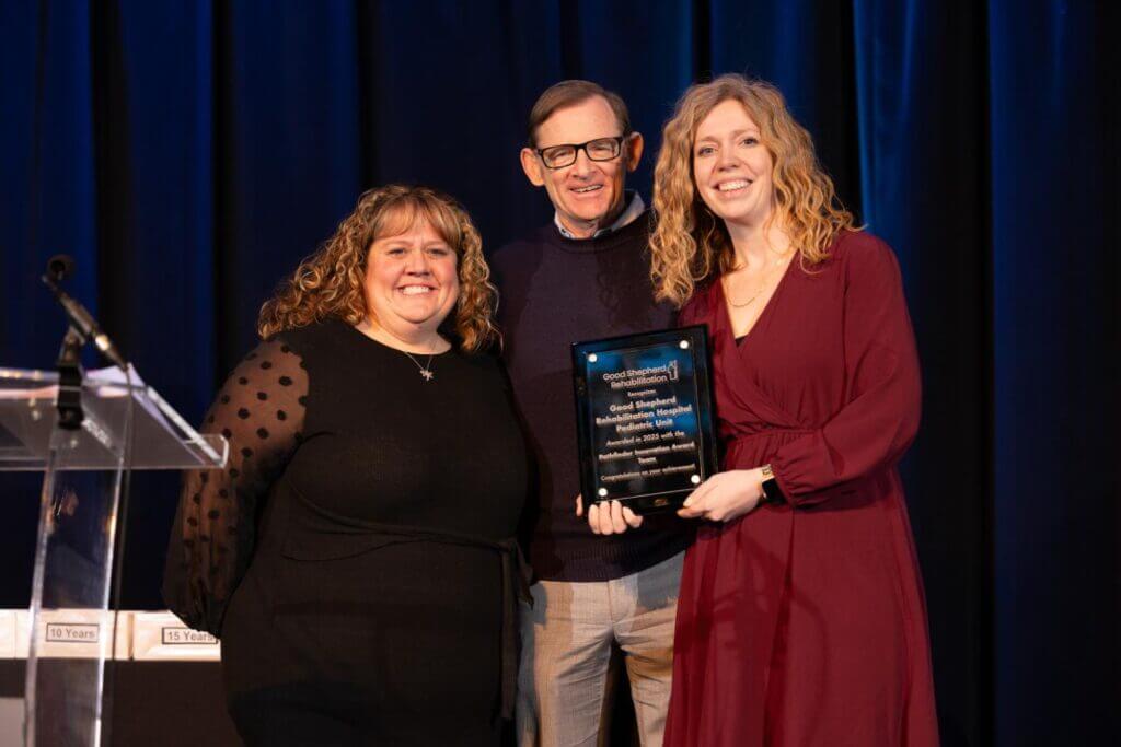 Dr. Kimberly Kuchinski (left), Michael Spigel (center) and Amanda Kleckner (right) pose for a photo while Amanda holds the Good Shepherd Rehabilitation Pathfinder Innovation Award