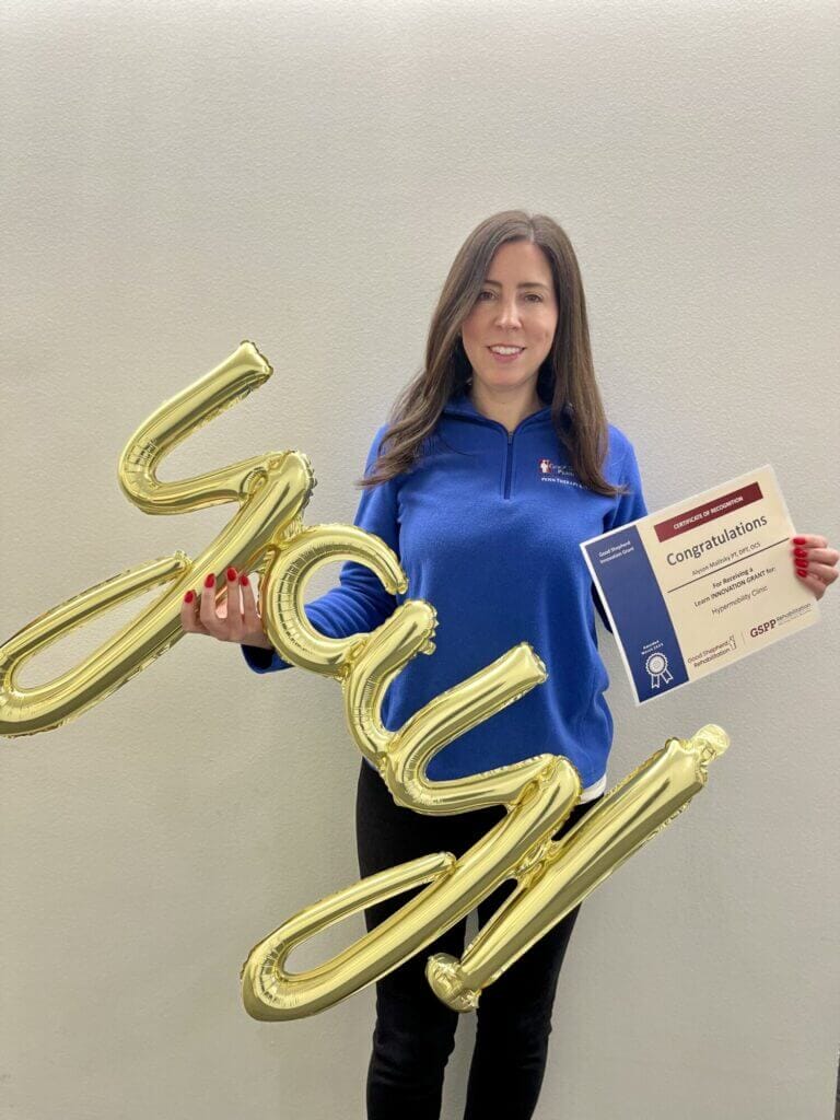 A person in a blue quarter-zip holds a balloon that reads "Yay!" and a certificate that reads "Congratulations"
