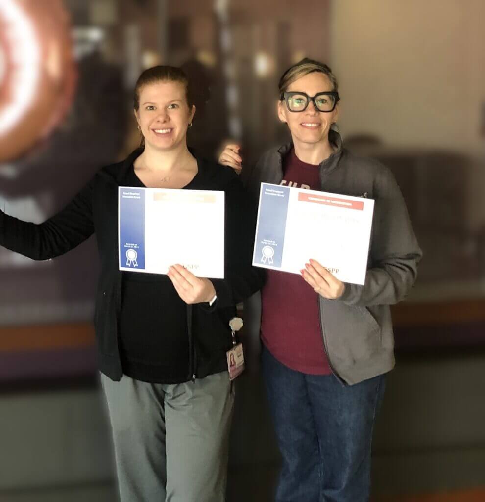 Two people smile while holding certificates.