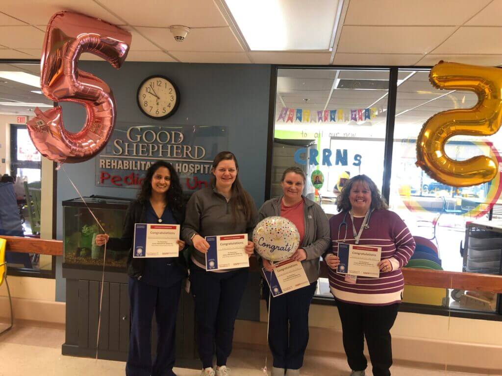 4 people are smiling while holding a certificate that reads "Congratulations" two balloons are at their side of the number 5.