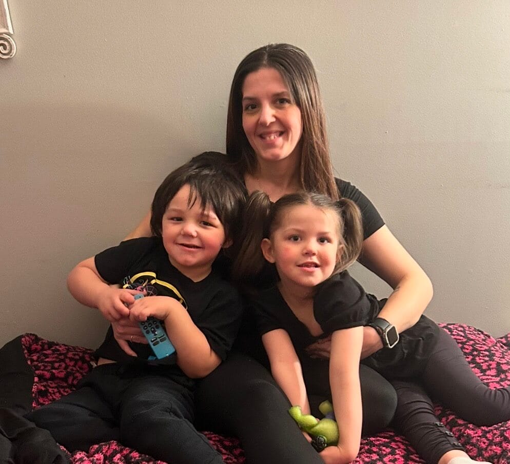 A mother sits in the middle of her two children, a son and daughter, and smile at the camera