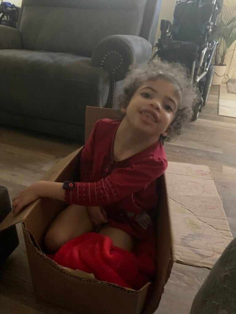 A child sitting in a cardboard box and smiling at the camera