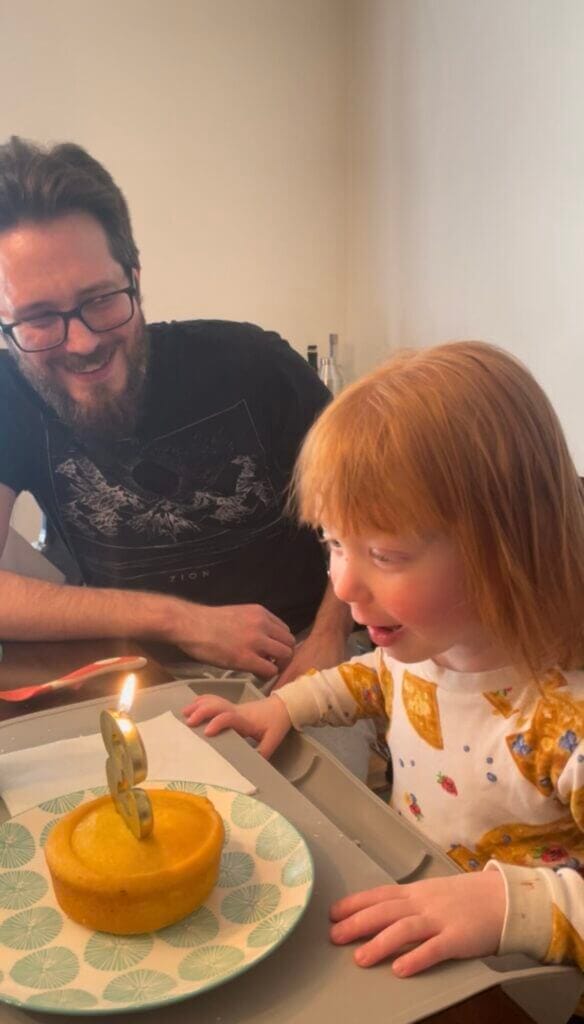 A young person blows out the candle on their 3rd birthday cake at home